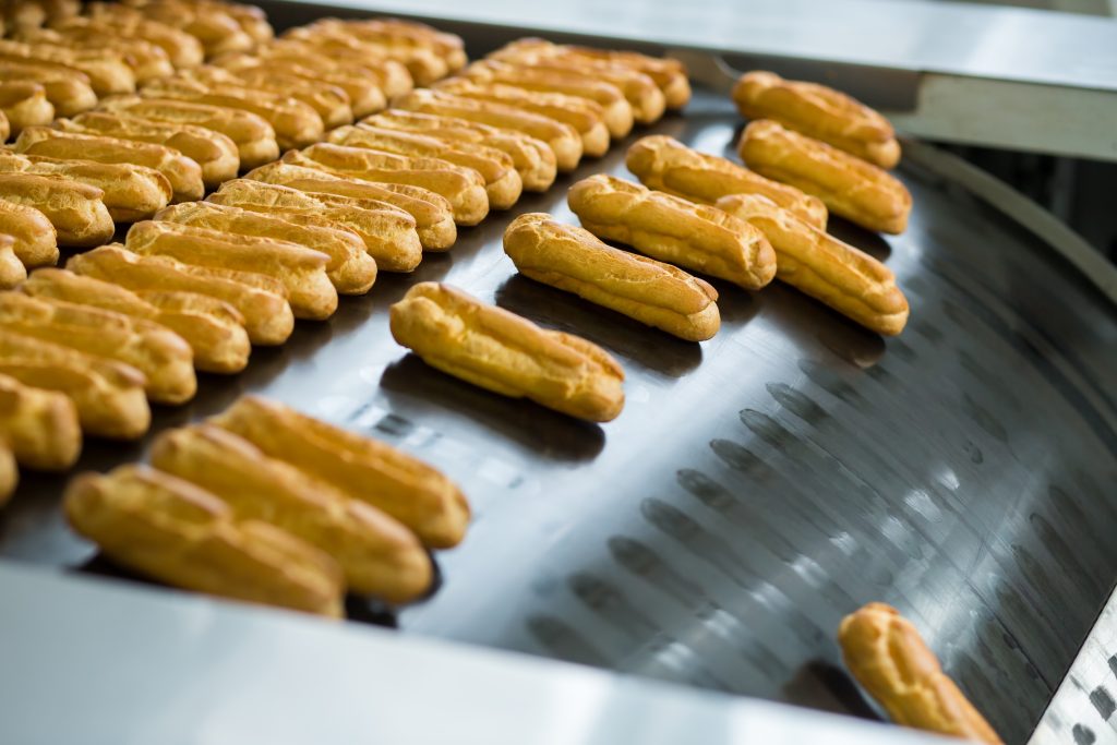 Yellow eclair shells on conveyor. Eclairs slide down conveyor line. High standard of quality. Making the best confectionery.
