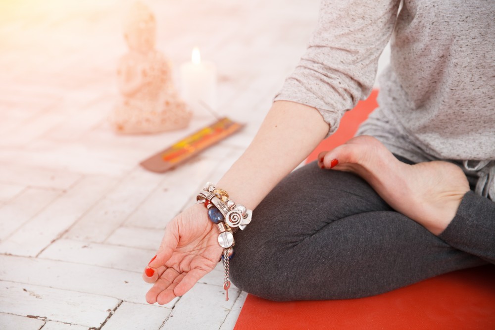 Woman sitting in lotus asana and doing yoga meditation with spiritual accessories, candles and Buddha statue. Concept of physical and mental health, relax and well being